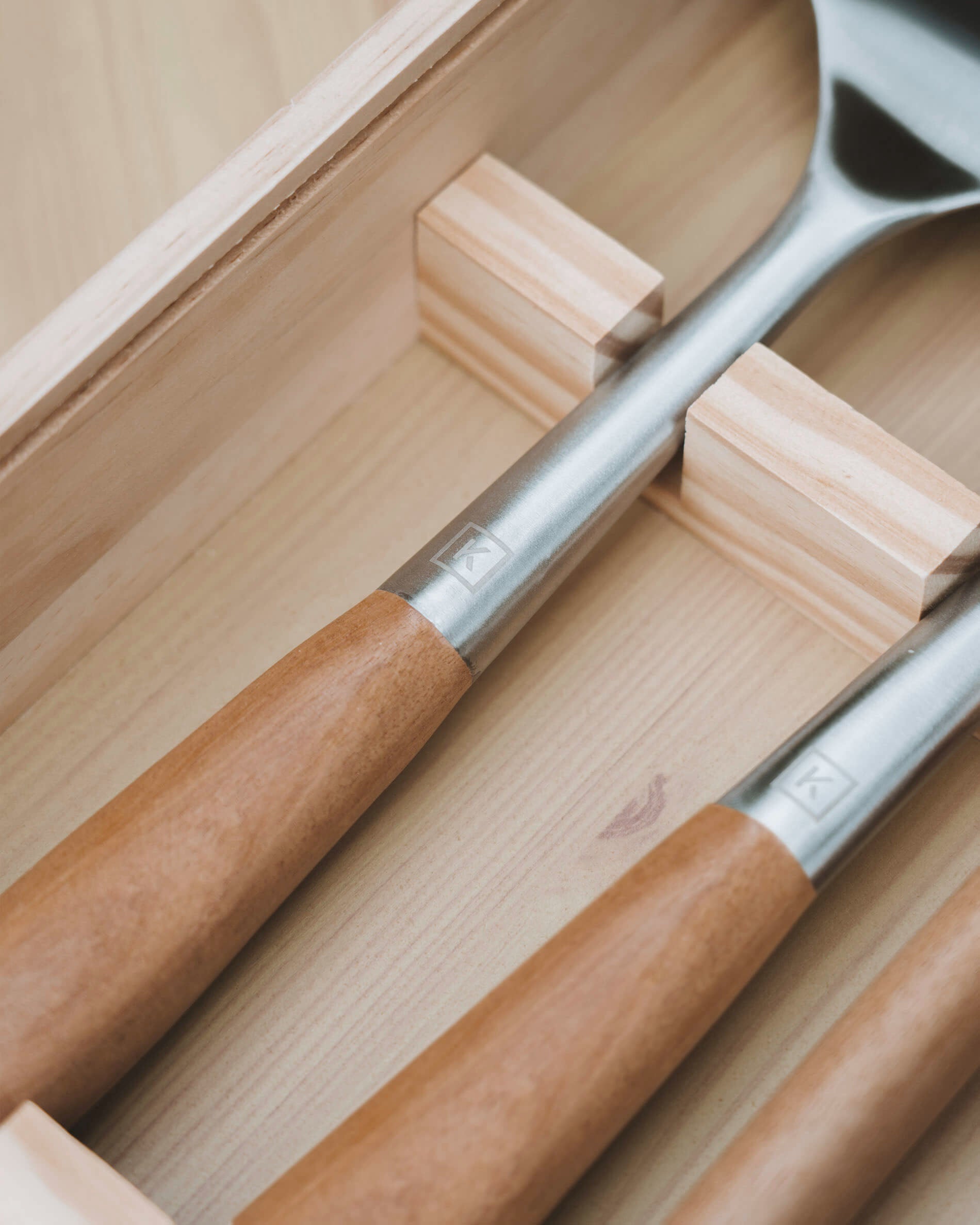 Detailansicht von Kochutensilien mit Griffen aus Akazienholz und Köpfen aus Edelstahl, ordentlich in einer unterteilten Holzbox aufbewahrt