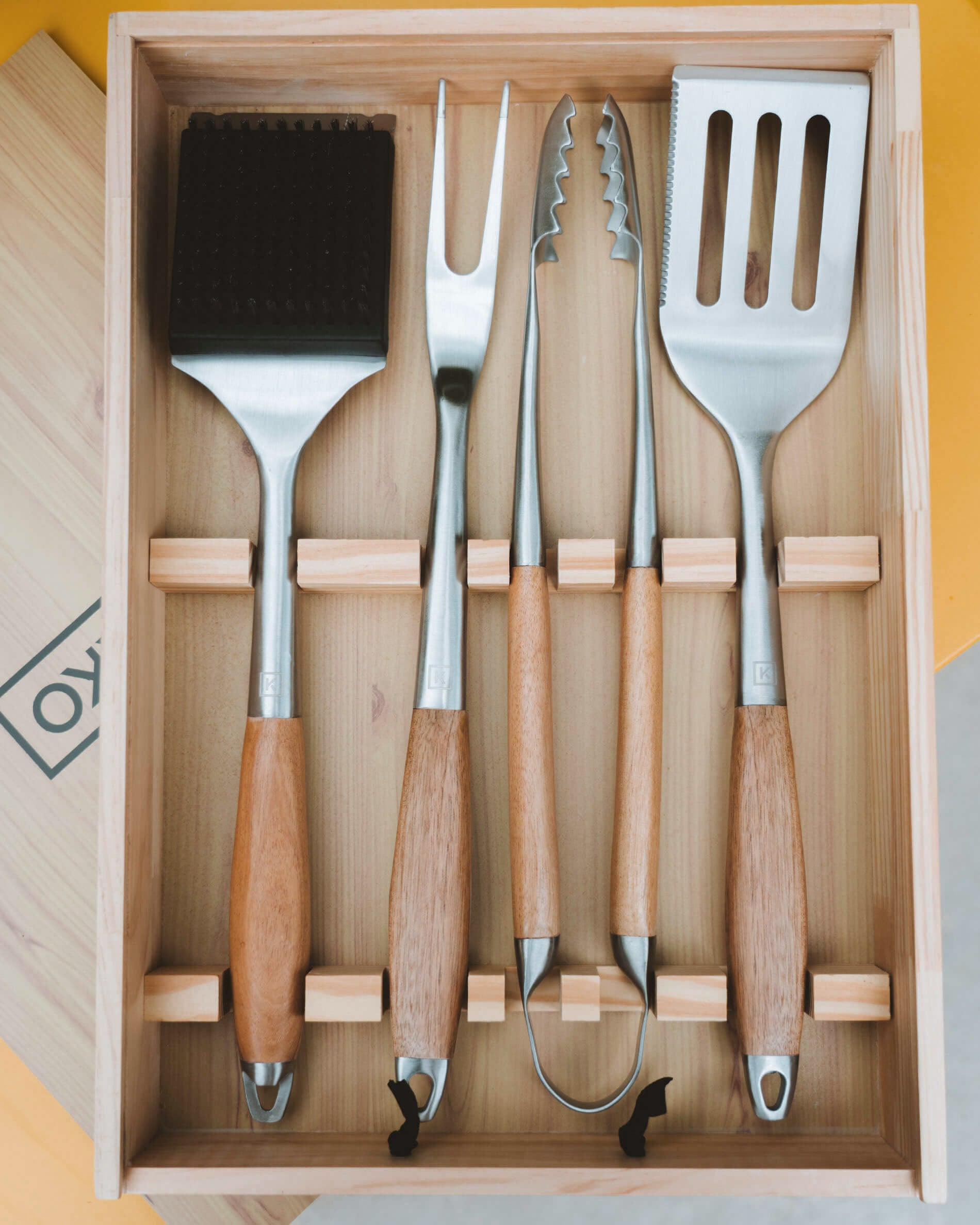Draufsicht auf eine Holzbox mit einem Set aus Edelstahl-Küchenutensilien mit Akazienholzgriffen, sorgfältig in Fächern angeordnet.