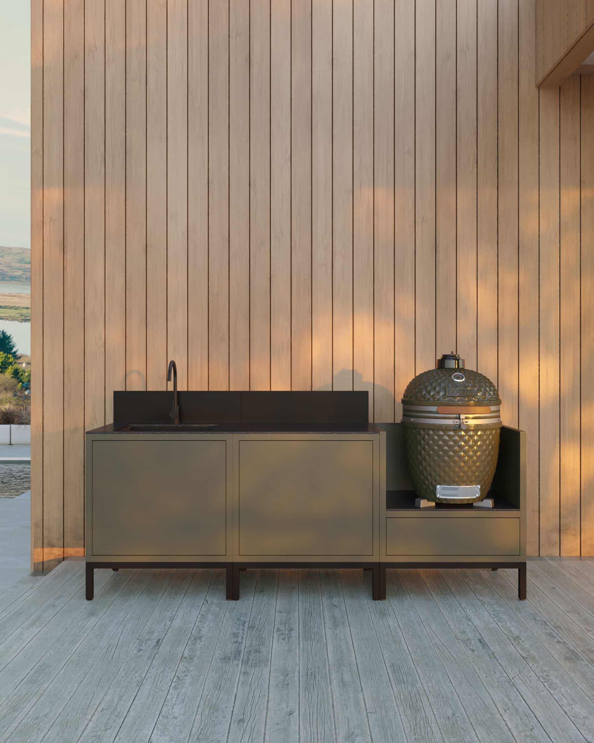 Cuisine pilotis 3 modules pour kamado avec évier intégré, meuble coloris olive avec plan de travail et crédence assortis, évier avec robinet à gauche, deux modules de rangement fermés au centre et kamado intégré dans le module latéral droit, structure sur pieds noirs, installation en extérieur contre un mur en bardage bois.