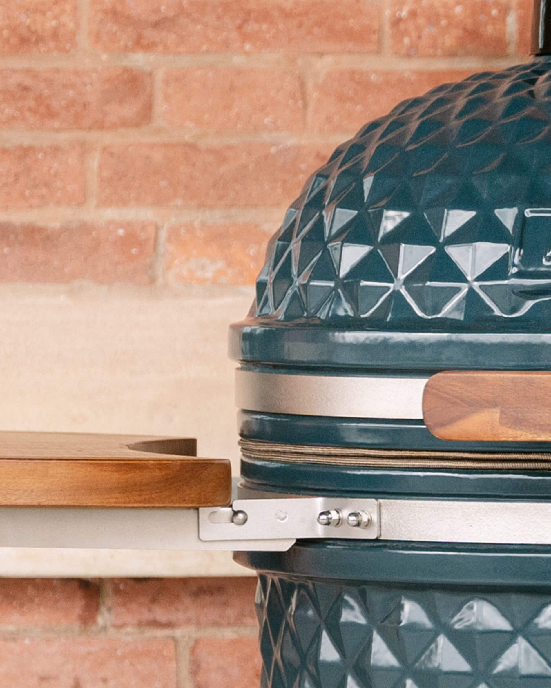 Detail der seitlichen Befestigung eines Holzablagebretts am Kamado Kokko, mit dem Metallsystem, das das Brett mit dem Keramikkorpus verbindet.