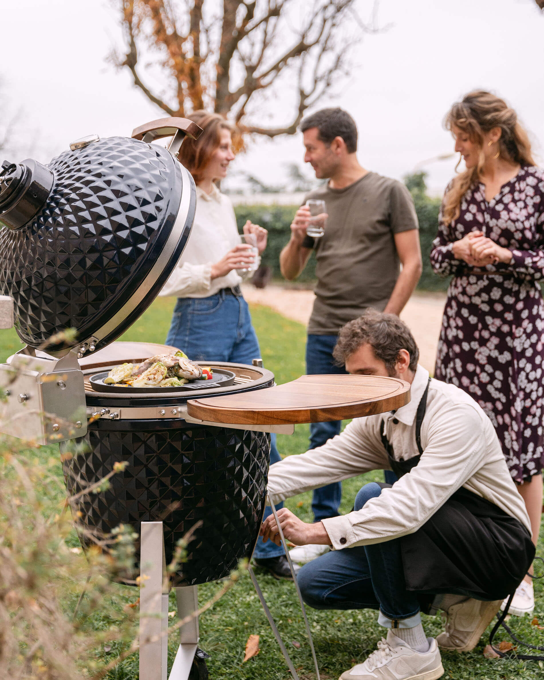 Kamado Kokko 22 pouces en céramique bleu marine utilisé lors d’un moment convivial en extérieur.