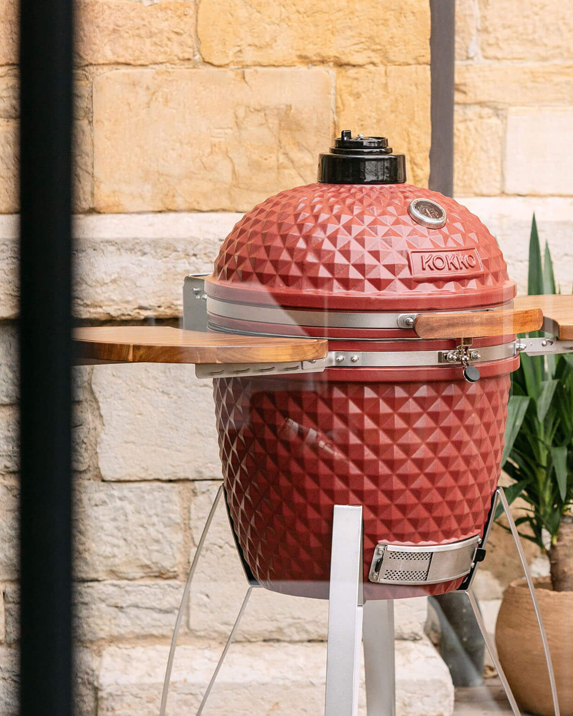 Barbecue kamado Kokko 22 pouces coloris rouge oxyde, présenté seul en extérieur.