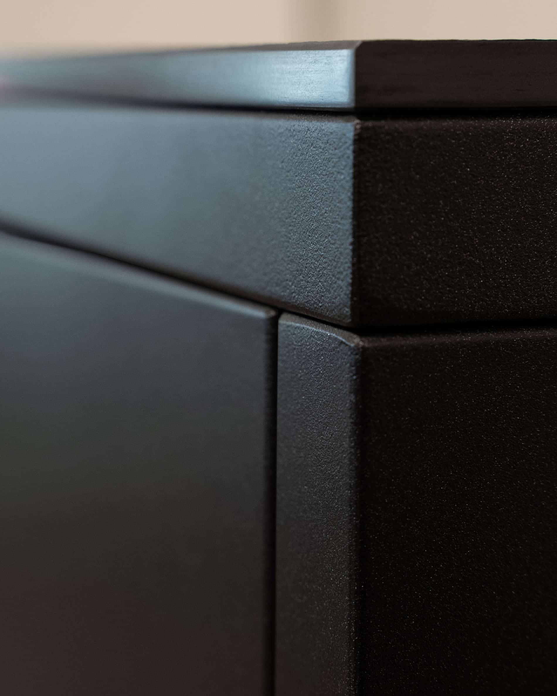 Détail de finition d’une cuisine pilotis, montrant l’angle du meuble, l’assemblage des panneaux et la texture mate de la façade sombre.
