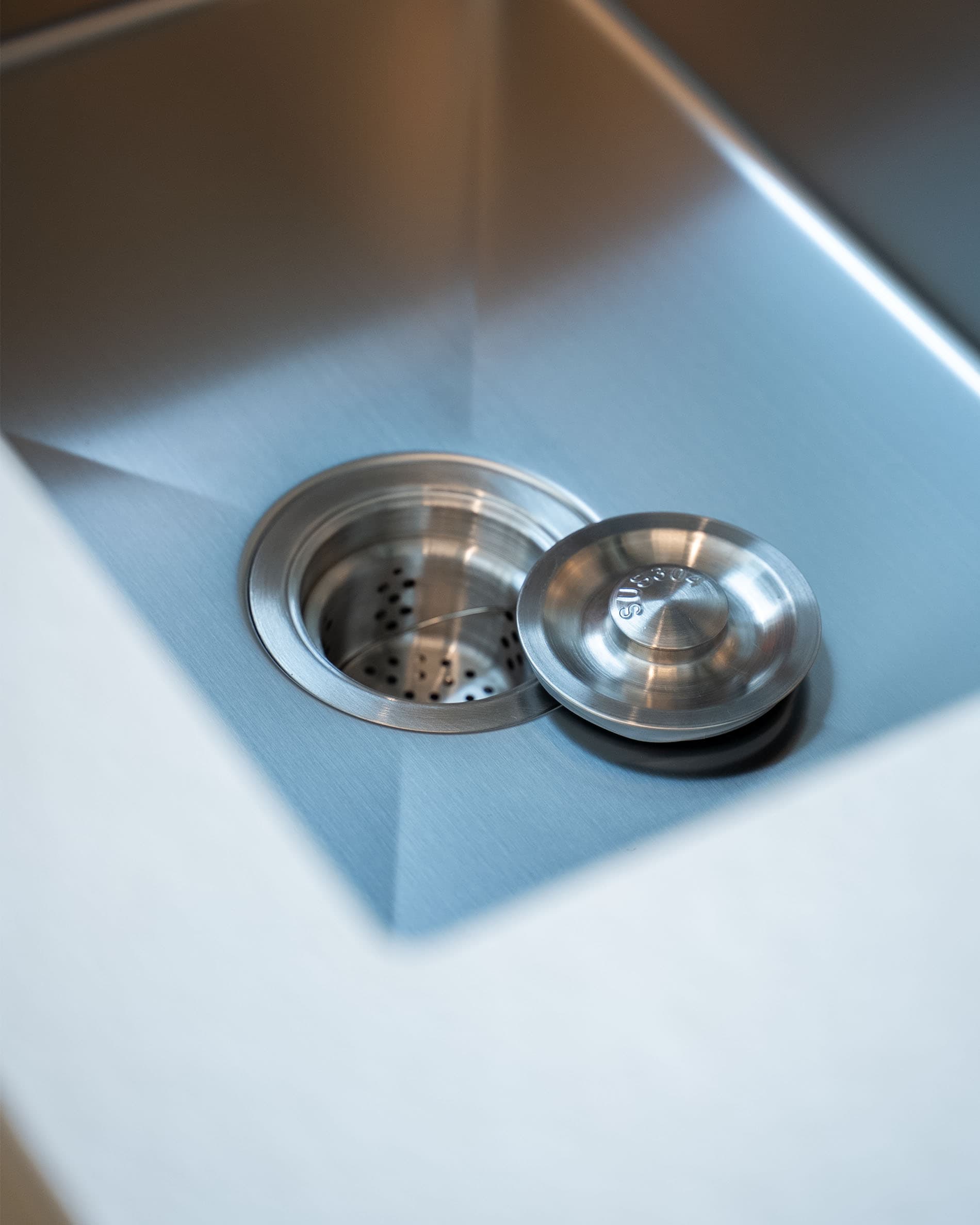 Détail de la bonde d’évier d’une cuisine pilotis, montrant le bac en inox et le système d’évacuation intégré.