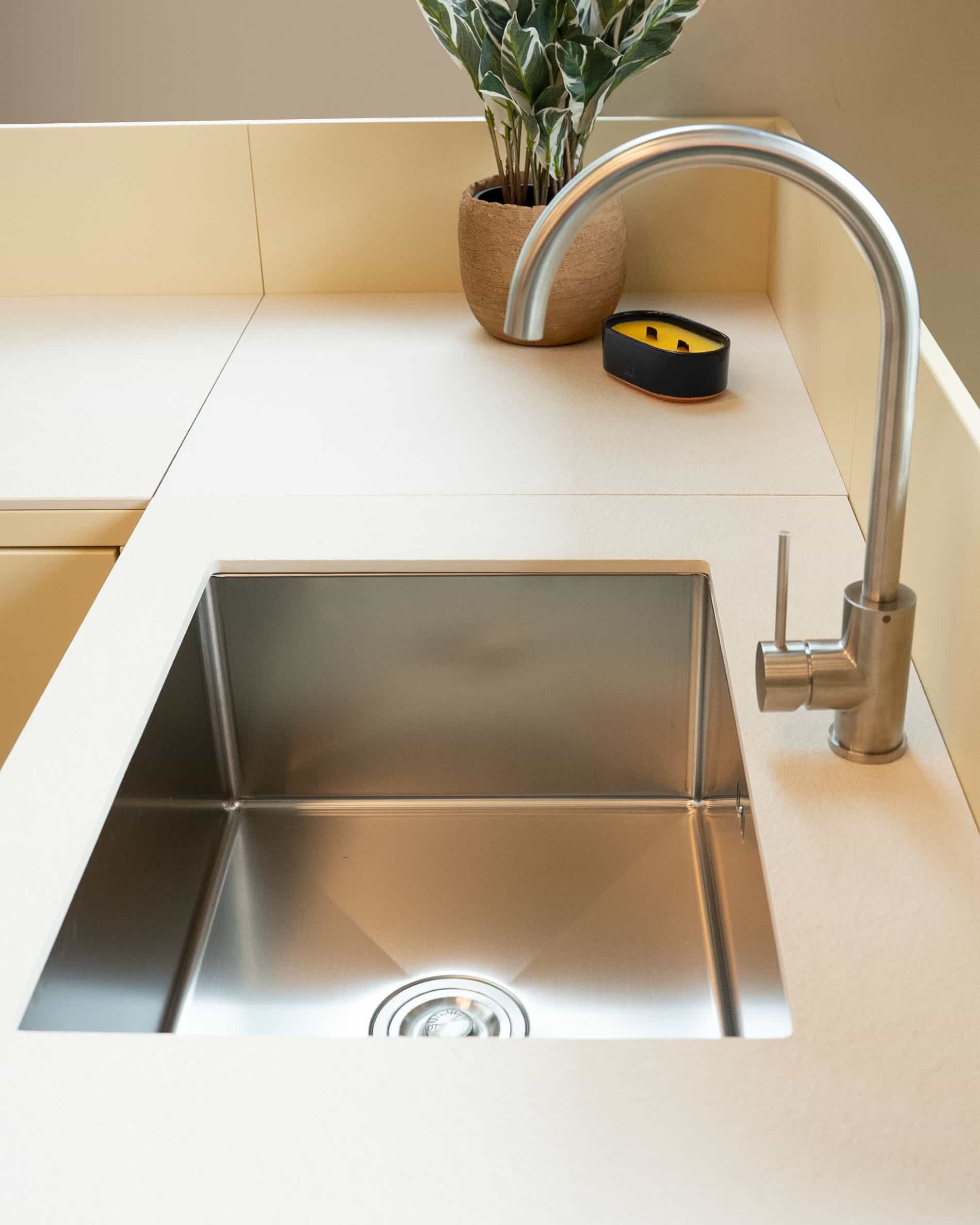 Détail de l’évier intégré d’une cuisine pilotis, avec bac en inox, robinetterie métallique et plan de travail crème.