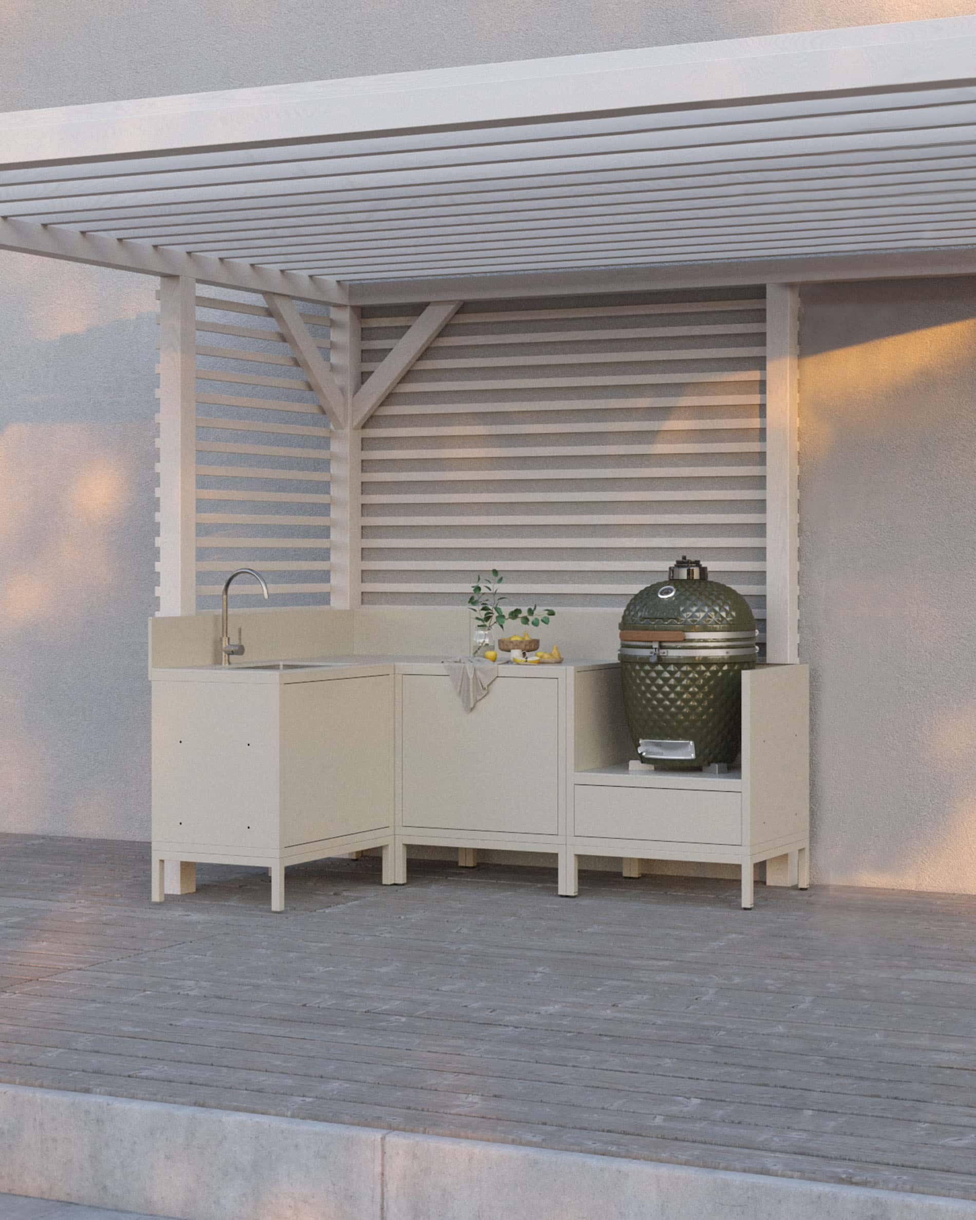Outdoor-Küche auf Stelzen in Cremefarbe, bestehend aus vier Modulen mit Ecke und Spülbecken, durchgehender Arbeitsplatte und einem speziellen Platz für den Kamado, installiert unter einer weißen Pergola auf einer Holzterrasse.