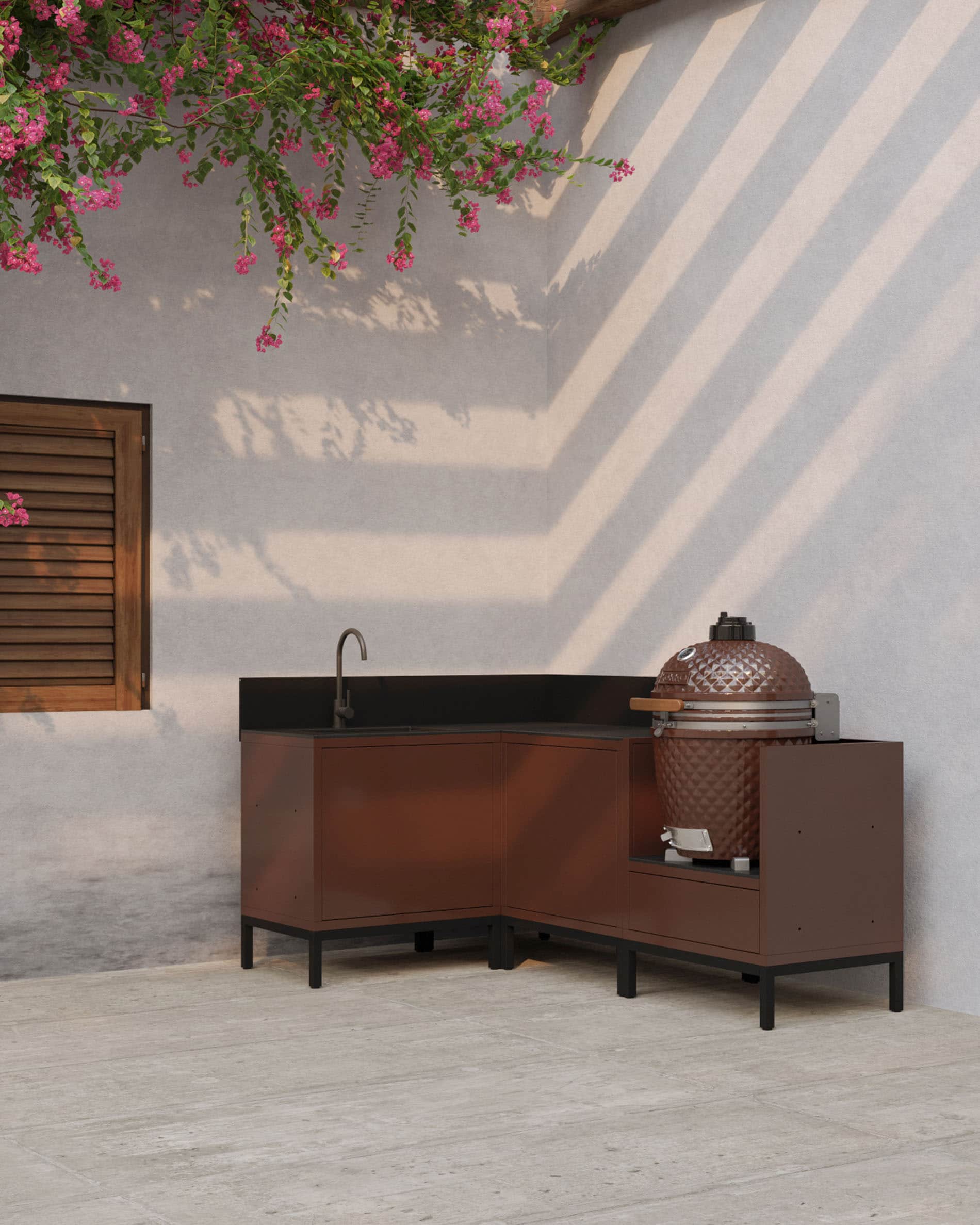 Cuisine pilotis d’angle coloris rouille avec plan de travail sombre, rangements fermés et module dédié à l’intégration d’un kamado en extérieur.