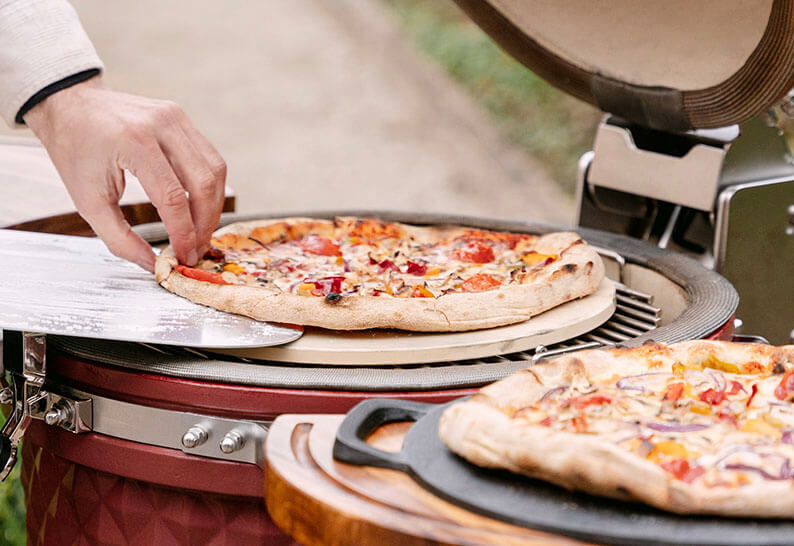Pizzas en cours de cuisson dans un kamado Kokko, montrant la cuisson indirecte sur pierre réfractaire.